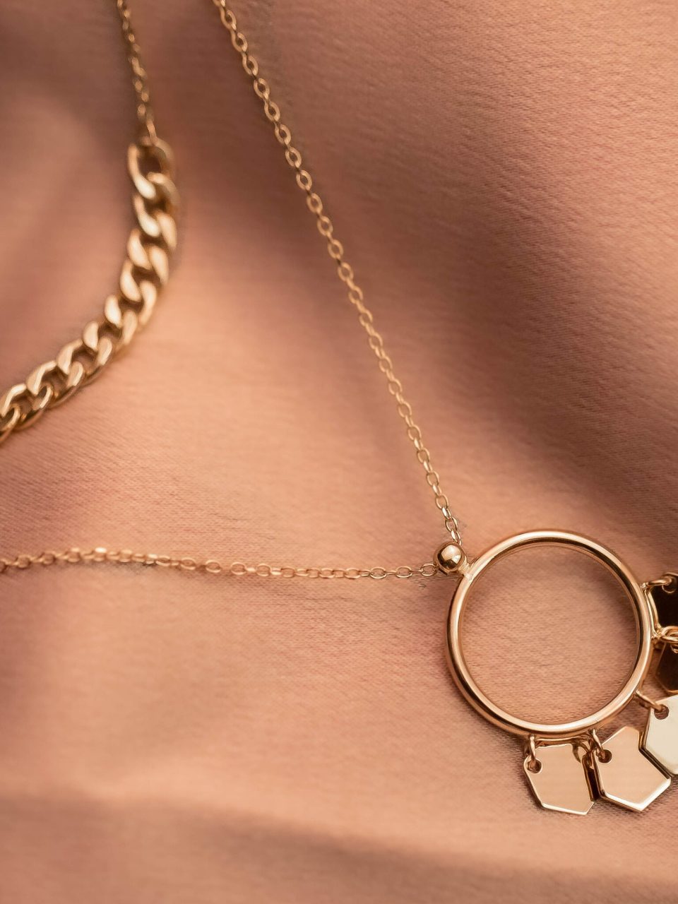 Close-up of a stylish gold necklace with hexagonal charms on textured fabric, showcasing elegance.