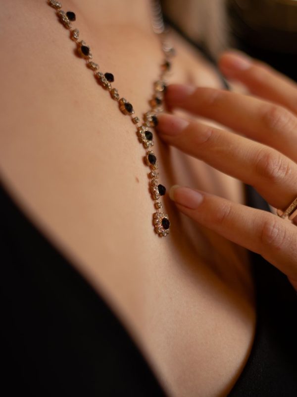 Close-up of a woman's hand touching a delicate beaded necklace draped elegantly over her neck.