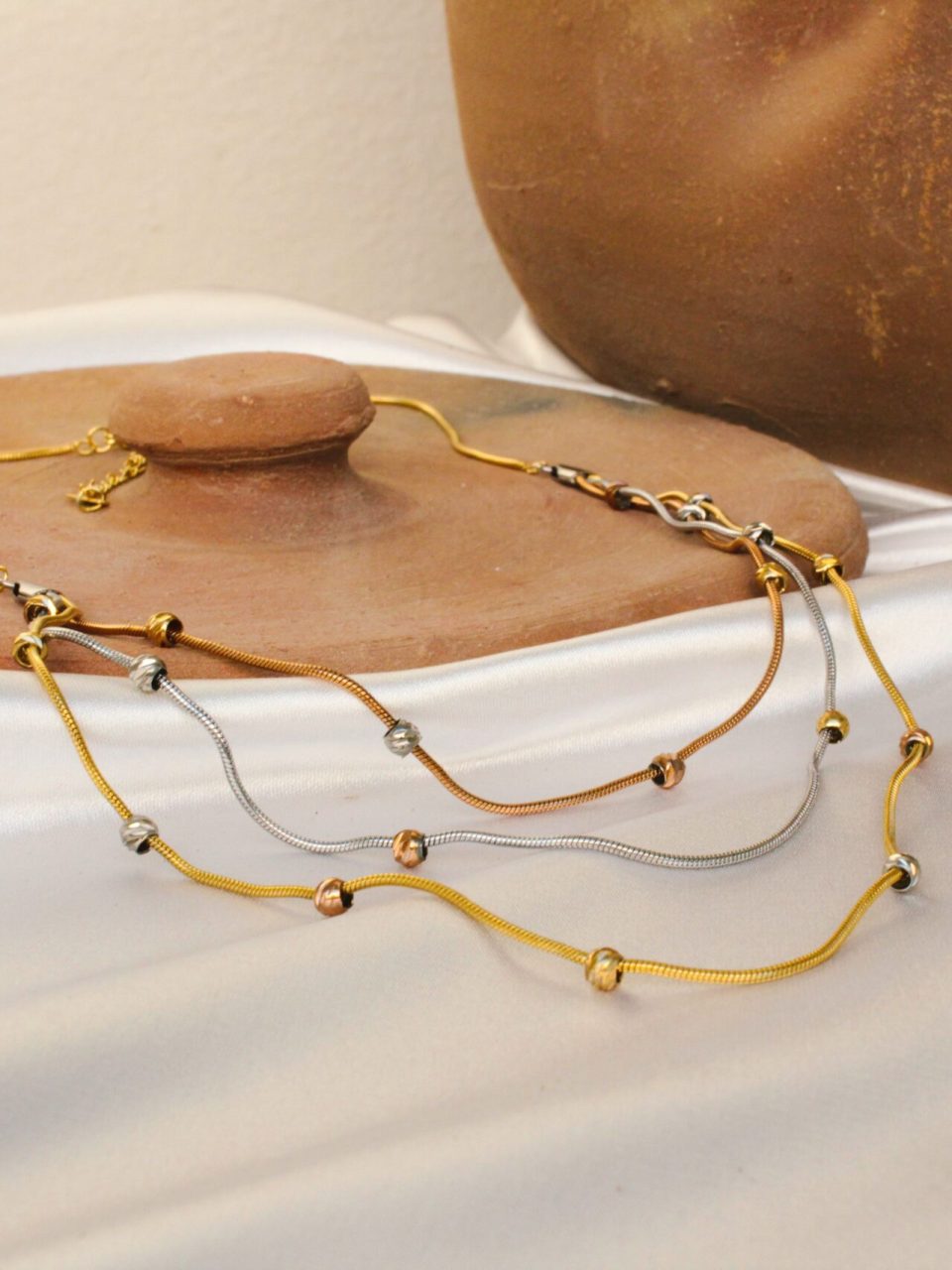 Stylish necklaces displayed elegantly on a white fabric with a rustic clay pot backdrop.