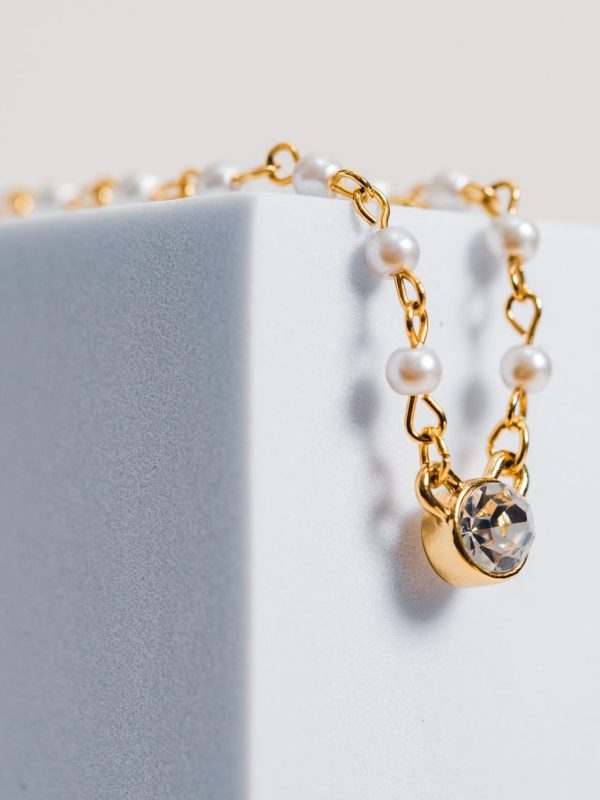 Close-up of a luxurious gold and pearl necklace delicately draped on a white block.